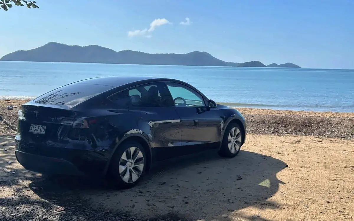 Black Tesla Model Y parked on the beach near Cairns with an island behind